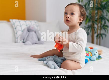 Adorable garçon hispanique assis sur le lit avec des poupées dans la chambre Banque D'Images