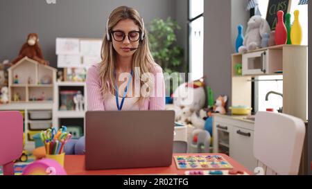 Jeune femme blonde enseignante utilisant un ordinateur portable travaillant à la maternelle Banque D'Images