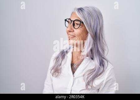 Femme d'âge moyen avec des tatouages portant des lunettes debout sur fond blanc regardant loin à côté avec le sourire sur le visage, expression naturelle. riant con Banque D'Images
