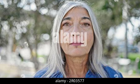 Femme d'âge moyen à cheveux gris debout avec une expression sérieuse au parc Banque D'Images