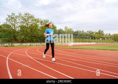 Une femme court sur une piste de course dans le stade en été. Banque D'Images