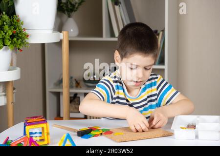 Un enfant d'âge préscolaire joue avec une mosaïque, construit des figures sur une planche, martelant des ongles avec un marteau sur des parties multicolores du concepteur Banque D'Images