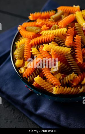 Pâtes rotini ou fusilli de trois couleurs sur une serviette en lin bleu. Pâtes italiennes crues colorées dans un bol sur des planches de bois. Gros plan Banque D'Images