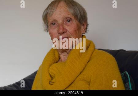 Portrait d'une femme âgée et détendue assise sur un canapé dans la salle de séjour. Pull à col roulé jaune et broche dorée Banque D'Images