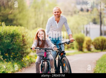 Portraits souriant père avec fille pendant l'été randonnée à vélo en plein air. Ils apprécient la convivialité dans le parc de la ville d'été. Bonne parentalité et chi Banque D'Images