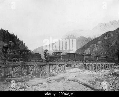 Le White Pass et le chemin de fer du Yukon traversent la rivière Skagway (21 octobre 1898). Pendant la ruée vers l'or du Klondike, le col blanc était l'un des itinéraires utilisés par les prospecteurs pour se rendre de Skagway aux champs aurifères du Yukon. En avril 1898, la White Pass and Yukon Railroad Company a été formée dans le but d'établir un chemin plus facile à travers le passage. La construction du chemin de fer a commencé le mois suivant. Des milliers de travailleurs ont travaillé 24 heures sur 24 dans des conditions dangereuses pour terminer le projet. La voie ferrée a été achevée au col blanc sur 20 février 1899 et a atteint le lac Bennett sur 6 juillet 1899. Banque D'Images