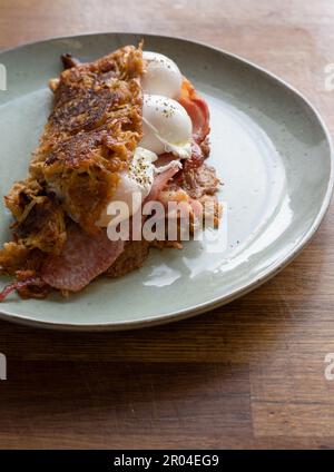 Offrez-vous ce délicieux et confortable plat de brunch composé de crêpes aux pommes de terre croustillantes, d'œufs parfaitement pochés et de bacon croustillant. La cuisson à la vapeur est chaude Banque D'Images