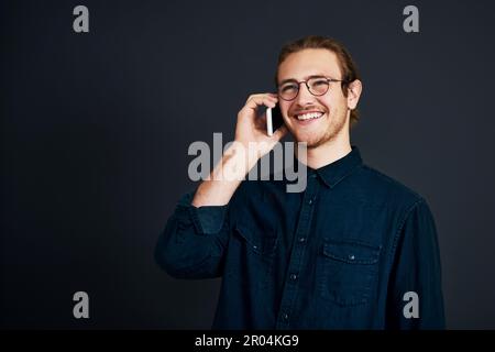 Conclure la vente par téléphone. un beau jeune homme d'affaires debout et parlant sur son téléphone portable sur fond noir dans le studio. Banque D'Images