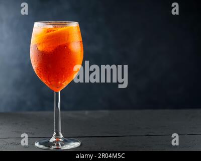 Apéritif Spritz cocktail en verre avec orange frais sur des planches de bois sombre. Un verre d'Aperol Spritz est servi dans un verre de vin. Copier l'espace Banque D'Images