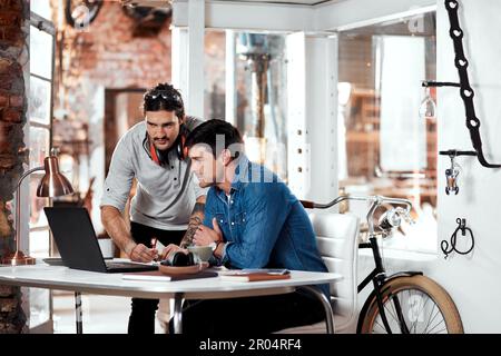 Eh bien, faites toujours le travail. deux jeunes hommes d'affaires travaillant ensemble sur un ordinateur portable dans un bureau à l'intérieur de leur atelier. Banque D'Images