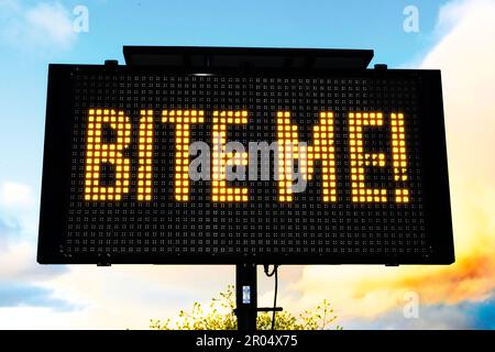 Un panneau de signalisation électronique affiche un message humoristique. Le panneau affiche « BITE ME! » dans des lumières orange-jaune vives disposées sur un fond noir. Banque D'Images