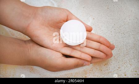 Femme tenant la bombe de bain sur l'eau avec de la mousse, gros plan Banque D'Images