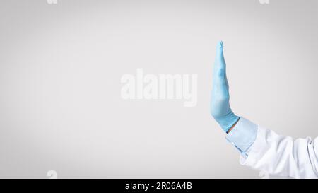 La main d'un médecin senior en manteau blanc avec des gants de protection montre un panneau stop avec la main Banque D'Images