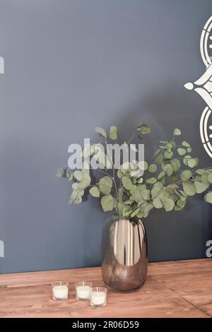 branches d'eucalyptus vert dans un vase sur une table à côté de trois bougies blanches en verres. décoration maison, verdure à la maison. Banque D'Images