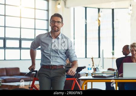 Conscient de la façon dont il se rend. Portrait d'un concepteur mature debout dans un bureau avec son vélo. Banque D'Images