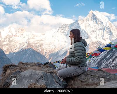 Une femelle routard assise dans le camp de base d'Annapurna méditant avec mala et Machhapuchhre chaîne en arrière-plan. Banque D'Images