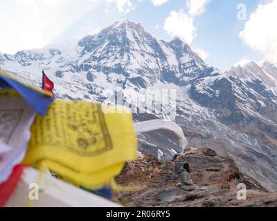 Drapeaux de prière et femme assise dans le camp de base d'Annapurna faisant une méditation pour remercier les esprits de la nature après tout l'effort qui a pris pour y arriver. Banque D'Images