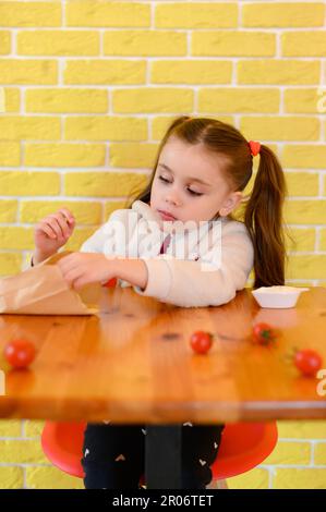 Portrait d'une petite fille mignonne mangeant des frites dans un restaurant de restauration rapide, mur jaune dans un café. Banque D'Images