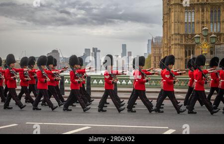 Portant leurs fusils, les soldats des Grenadier Guards de l'armée britannique défilent en costume de cérémonie sur le pont de Westminster et au-delà des maisons Banque D'Images