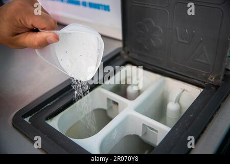 Gros plan sur les mains d'un homme qui verse du détergent en poudre dans le lave-linge de la buanderie Banque D'Images