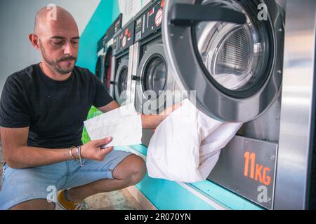 Un homme insère les feuilles d'absorbeur de couleur dans la machine à laver pour laver des vêtements Banque D'Images