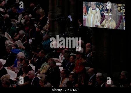 Le roi Charles III porte la couronne St Edward comme il est projeté sur un grand écran lors de sa cérémonie de couronnement à l'abbaye de Westminster à Londres. Date de la photo: Samedi 6 mai 2023. Banque D'Images