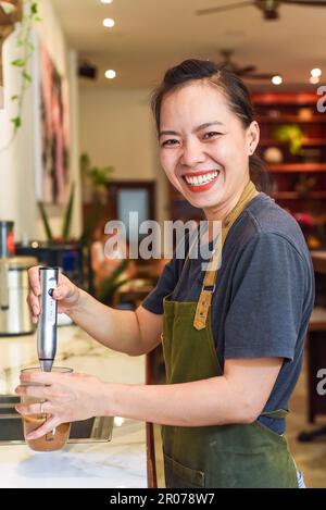 Barista vietnamien utilisant un batteur pour le lait condensé dans une tasse en verre pour préparer le café vietnamien SUA Banque D'Images
