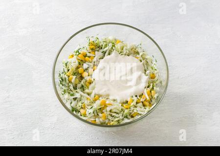 Bol en verre avec salade de chou blanc, maïs doux, œuf, aneth et oignon vert avec sauce sur fond gris clair, vue du dessus. Stade de cuisson Banque D'Images