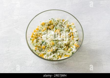 Bol en verre avec salade de chou blanc, maïs doux, œuf, aneth et oignon vert avec sauce sur fond gris clair, vue du dessus. Stade de cuisson Banque D'Images