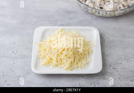Planche en bois avec tête coupée de fromage blanc, ail haché et épices sur fond gris clair. Étape de la cuisson d'un délicieux en-cas de vacances Banque D'Images