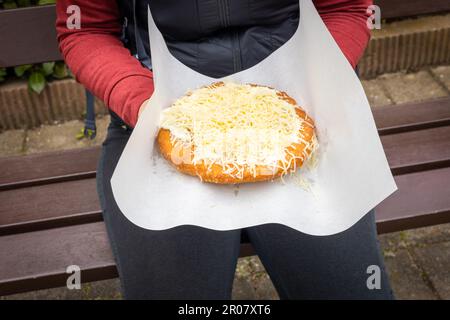 Femme tenant une langouse traditionnelle entre ses mains, assise sur un banc de parc, Langos, une pâtisserie frite populaire en Europe de l'est, servie avec des garnitures Banque D'Images