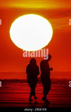 Isle of Palms, États-Unis d'Amérique. 07 mai 2023. Un couple est silhoueté alors qu'ils marchent le long de la plage vers un lever de soleil se présentant comme une balle géante, 7 mai 2023 à l'île des palmiers, en Caroline du Sud. La région de Charleston connaît un temps exceptionnellement frais et sec pour le mois de mai alors que le jet stream s'est plongé vers le sud, apportant de l'air canadien plus frais au sud-est des États-Unis, mais devrait revenir à la haute des années 80 plus tard dans la semaine. Crédit : Richard Ellis/Richard Ellis/Alay Live News Banque D'Images