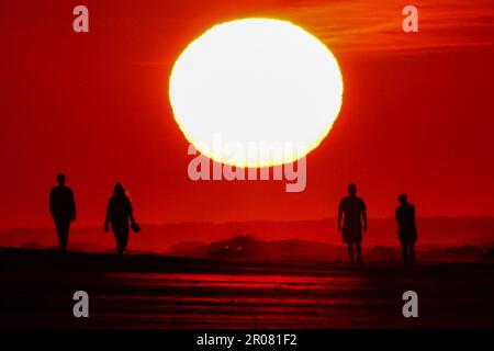 Isle of Palms, États-Unis d'Amérique. 07 mai 2023. Les gens sont silhouettés lorsqu'ils marchent le long de la plage vers un lever de soleil se présentant comme une balle géante, 7 mai 2023 à l'île des palmiers, en Caroline du Sud. La région de Charleston connaît un temps exceptionnellement frais et sec pour le mois de mai alors que le jet stream s'est plongé vers le sud, apportant de l'air canadien plus frais au sud-est des États-Unis, mais devrait revenir à la haute des années 80 plus tard dans la semaine. Crédit : Richard Ellis/Richard Ellis/Alay Live News Banque D'Images