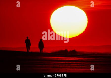 Isle of Palms, États-Unis d'Amérique. 07 mai 2023. Un couple est silhoueté alors qu'ils marchent le long de la plage vers un lever de soleil se présentant comme une balle géante, 7 mai 2023 à l'île des palmiers, en Caroline du Sud. La région de Charleston connaît un temps exceptionnellement frais et sec pour le mois de mai alors que le jet stream s'est plongé vers le sud, apportant de l'air canadien plus frais au sud-est des États-Unis, mais devrait revenir à la haute des années 80 plus tard dans la semaine. Crédit : Richard Ellis/Richard Ellis/Alay Live News Banque D'Images