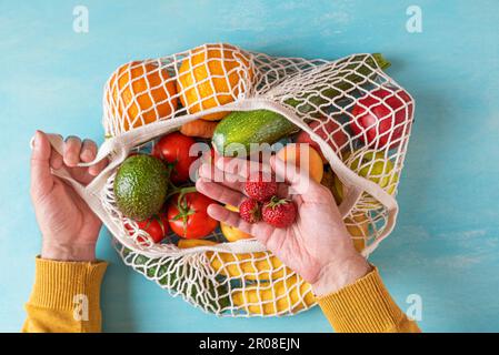 Homme poignet prenant des fraises du sac à provisions de filet avec des fruits et des légumes. Mode de vie durable, concept zéro déchet Banque D'Images