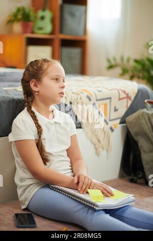 Fille fatiguée après avoir fait des devoirs assis sur le sol dans sa chambre à coucher Banque D'Images
