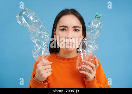 Thinking Angry girl, montre deux bouteilles, recyclage du plastique, passe vert, réutilisable déchets, arrière-plan bleu Banque D'Images