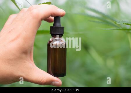 Mains tenant bouteille marron d'huile de cannabis, gros plan, plante laisse toile de fond. Banque D'Images