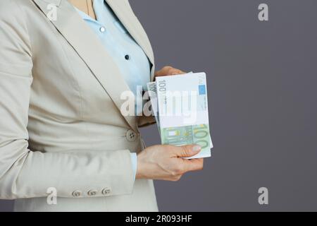 Gros plan sur une femme dans un costume d'affaires léger avec des packs d'euros sur fond gris. Banque D'Images