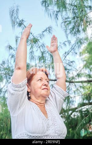 Femme hispanique senior vêtue de vêtements blancs pratiquant le yoga à l'extérieur dans un parc. Concepts : bien-être, mode de vie actif et sain. Banque D'Images