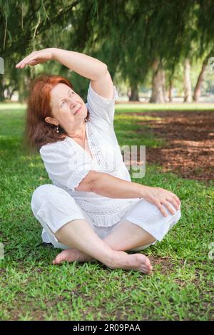 Portrait d'une femme hispanique âgée vêtue de vêtements blancs pratiquant le yoga à l'extérieur dans un parc. Concepts : bien-être, vitalité, mode de vie actif et sain. Banque D'Images