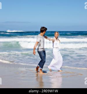 Juste un autre jour au paradis quand ils étaient ensemble. un jeune couple heureux qui profite d'une promenade le long de la plage. Banque D'Images