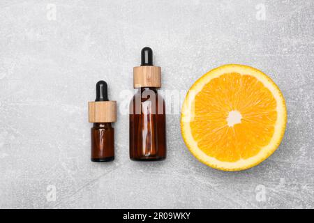 Bouteilles d'huile essentielle avec tranche d'orange sur la table grise, à plat Banque D'Images