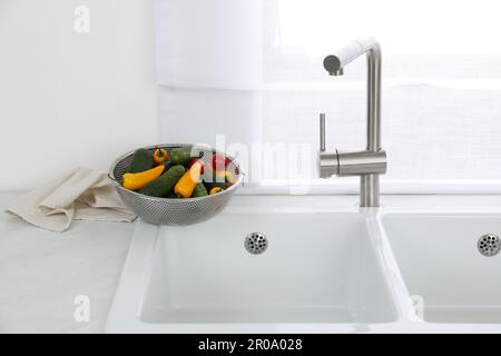 Évier moderne avec robinet d'eau et légumes frais près de la fenêtre dans la cuisine Banque D'Images