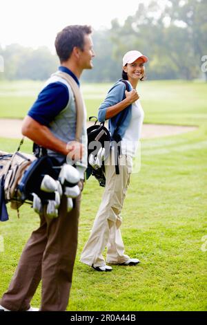Couple marchant sur le terrain de golf avec des sacs de golf. Couple transportant des sacs de golf et marchant sur le parcours de golf. Banque D'Images