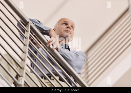 l'homme qui se penche contre la rambarde moderne observe sérieusement ce qui se passe au loin. Il est expérimenté et sait quoi faire. Il semble étrange à h. Banque D'Images