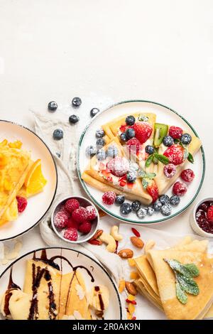 Variété de crêpes fraîches avec chocolat, confiture, fruits et baies sur fond blanc. Crêpes maison délicieuses. Vue de dessus. Copier l'espace. Banque D'Images
