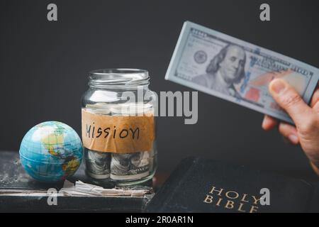 Sauver des bocaux pleins d'argent et de globe avec la Sainte Bible pour la mission, Mission christian idée. Main tenant dollar avec la bible sur table en bois, bac chrétien Banque D'Images