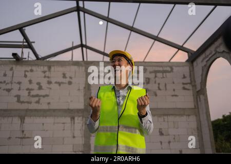 Ingénieur asiatique en uniforme et casque sur le chantier de construction étant heureux et souriant pour le succès. Projet réussi et expression du bonheur après le travail concept Banque D'Images