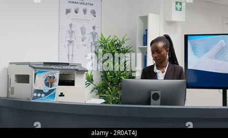 Réceptionniste répondant à un appel téléphonique sur ligne fixe au comptoir du hall, travaillant à l'hôpital pour aider les patients. Jeune adulte, téléphone avec cordon à la réception du centre de santé. Banque D'Images